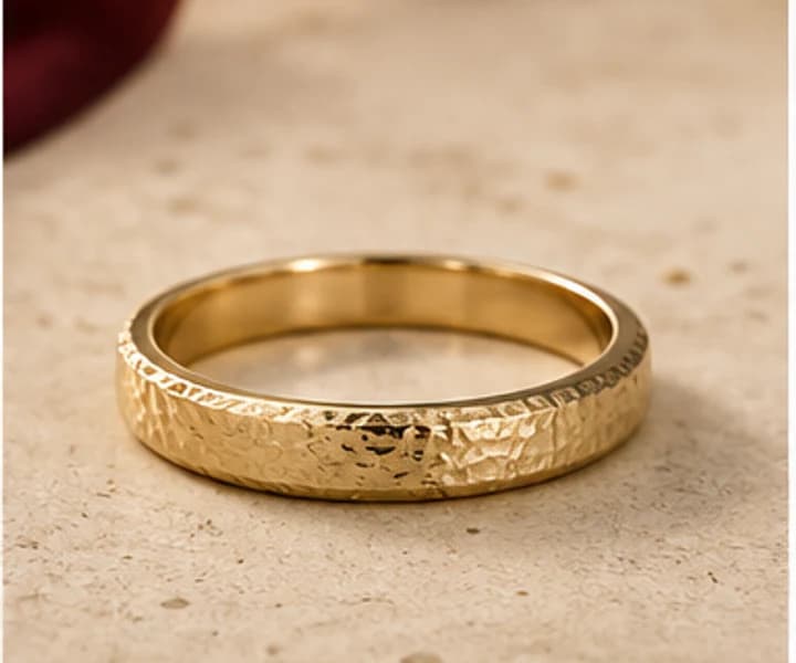 Illustrative textured gold wedding band on warm ivory stone