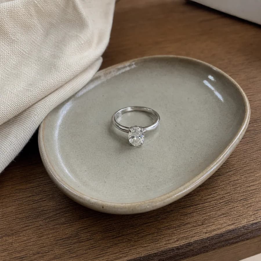 A refined oval engagement ring held in warm natural light.