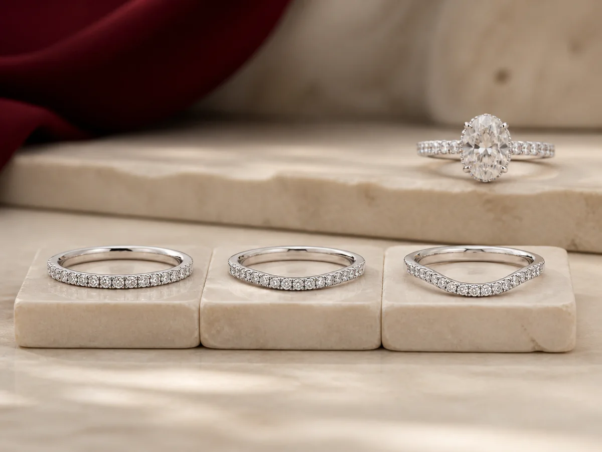 Three separate white-metal wedding bands with straight, gently curved, and deeper sculptural contour silhouettes below an oval engagement ring.